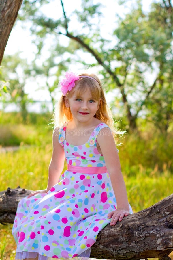 Little girl sitting on a tree branch in a summer park