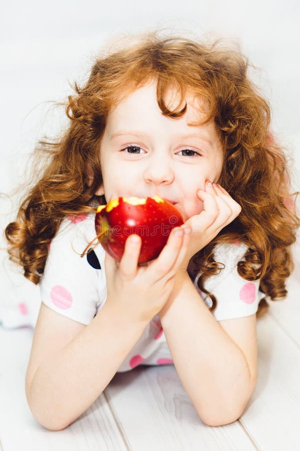 Little girl smiling and eating a red apple