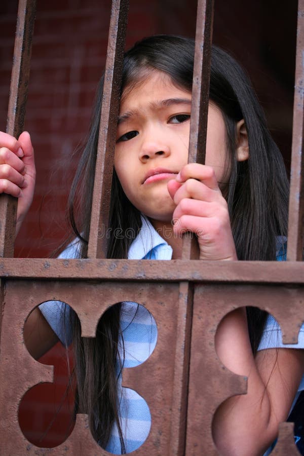 Little girl standing behind iron bars stock photo Little girl standing behind iron bars stock photo