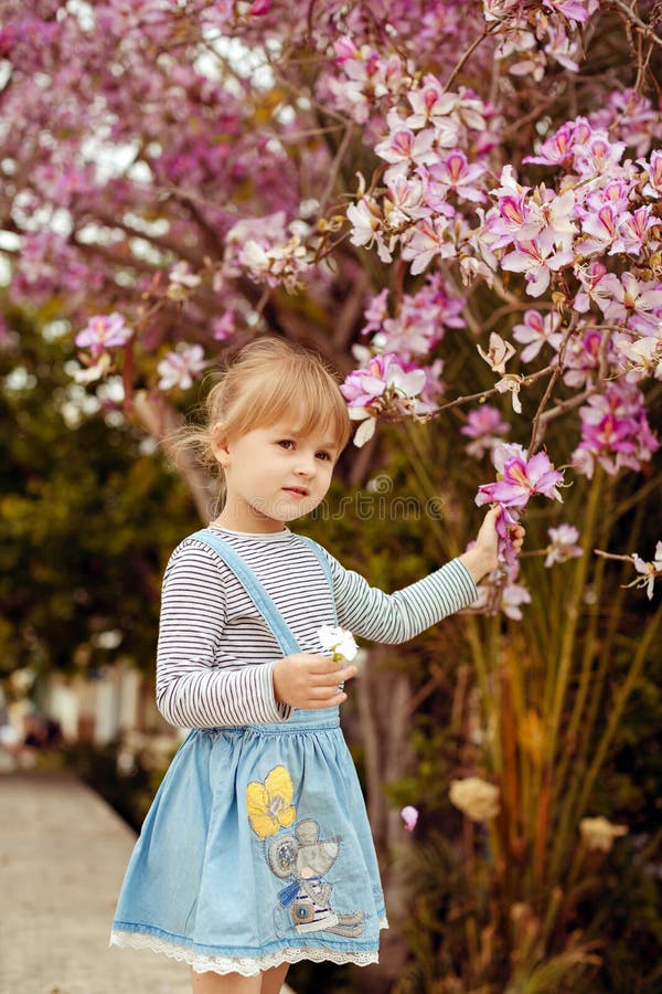 Little girl in a striped denim dress standing near a blossoming