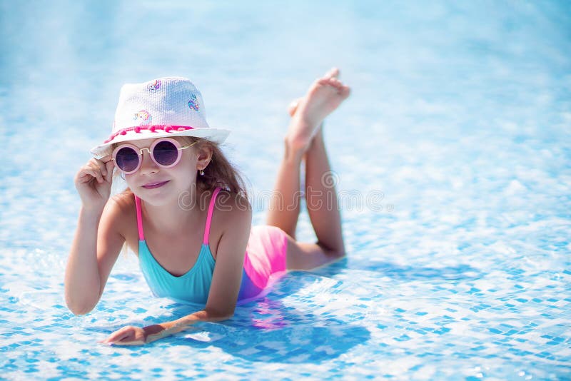 Little girl in Sunglasses and hat with unicorn in outdoor swimming pool of luxury resort on summer vacation on tropical beach island. Healthy outdoor sport activity for children. Kids beach fun