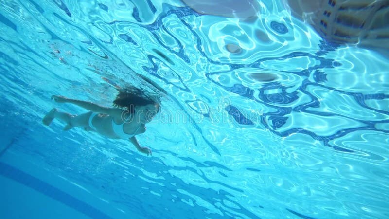 Fetița înoată în piscina albastră, cu fața în jos, cu fața în jos. stock video footage