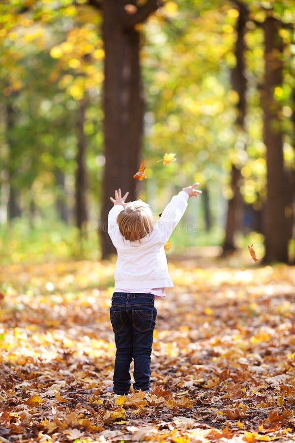 Little girl throwing leaves in the forest
