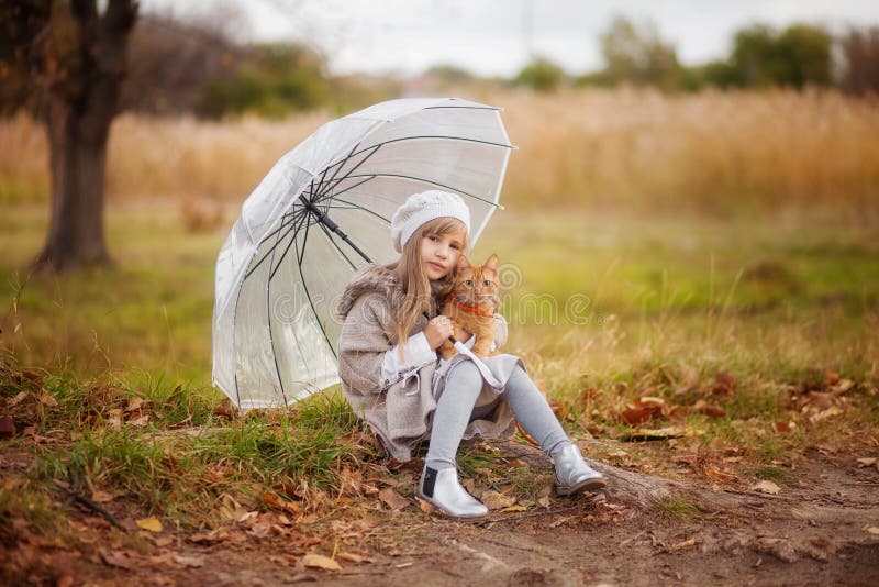 Little girl in vintage clothes with a red cat and a transparent umbrella on a walk in the autumn park