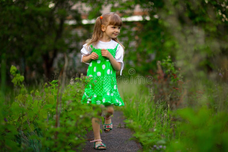 Little girl walk in green garden in summer day