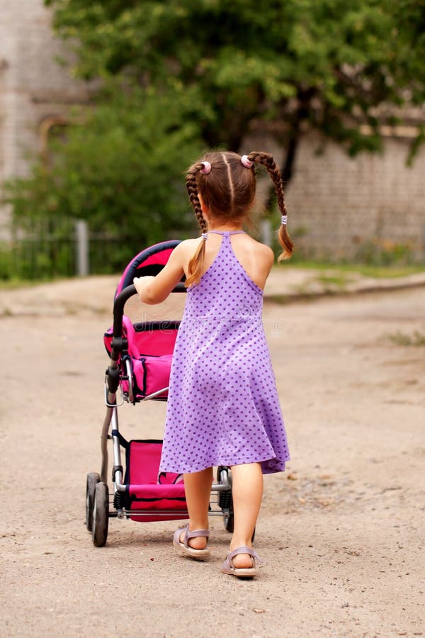 Little girl walking with toy stroller. Little Mama.