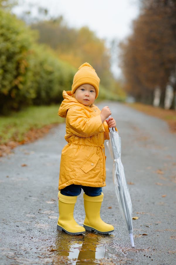 A Little Girl is Jumping in a Puddle in Yellow Rubber Boots and a ...