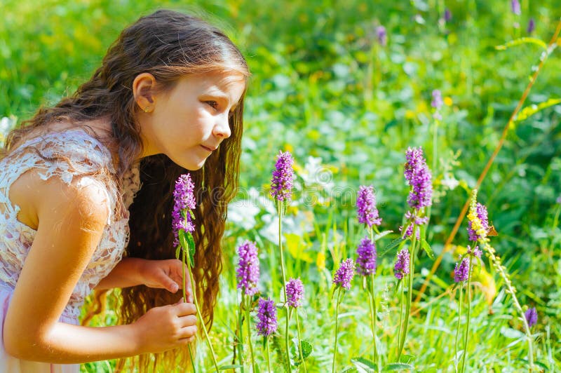 little girl watching a bee pollinate wild flowers in a field