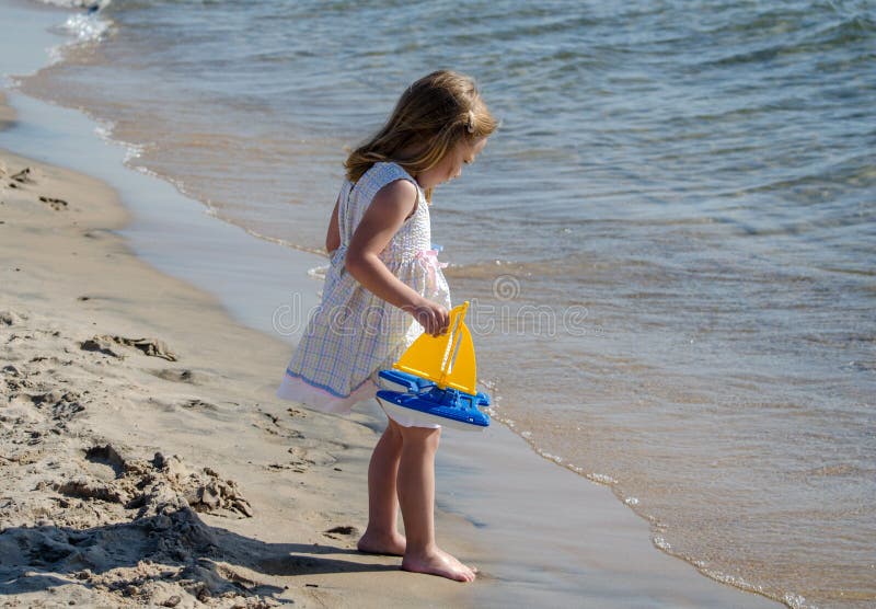 Little girl by the water with toy boat stock image Little girl by the water with toy boat stock image