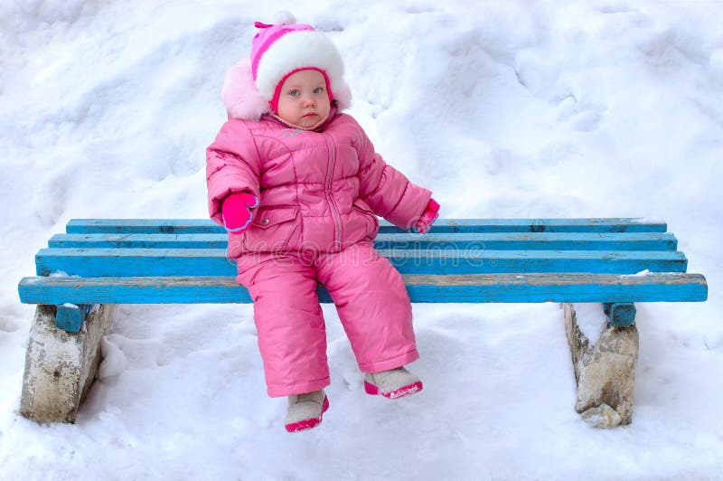 Little girl in winter outerwear sit on bench.