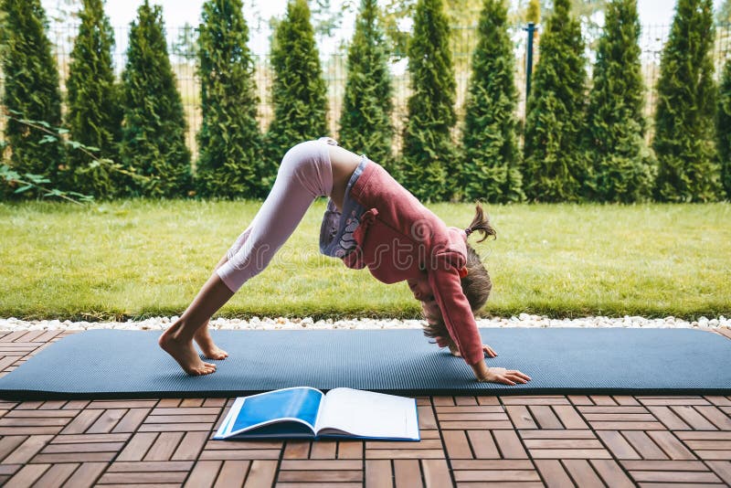 Little girl 5-6 years standing in the Downward Facing Dog position while practicing yoga outdoors