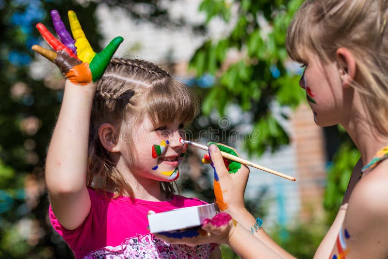 Little happy sisters play with colors in the park, children play, children paint each other