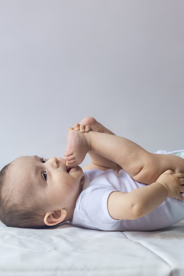 Little hungry baby boy taking feet in mouth. 6-month baby having fun in white bedding. Cute baby lying on bed. Family, new life, royalty free stock image Little hungry baby boy taking feet in mouth. 6-month baby having fun in white bedding. Cute baby lying on bed. Family, new life, royalty free stock image