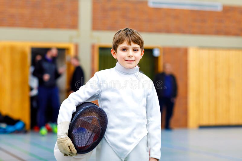 Little kid boy fencing on a fence competition. Child in white fencer uniform with mask and sabre. Active kid training stock photo Little kid boy fencing on a fence competition. Child in white fencer uniform with mask and sabre. Active kid training stock photo