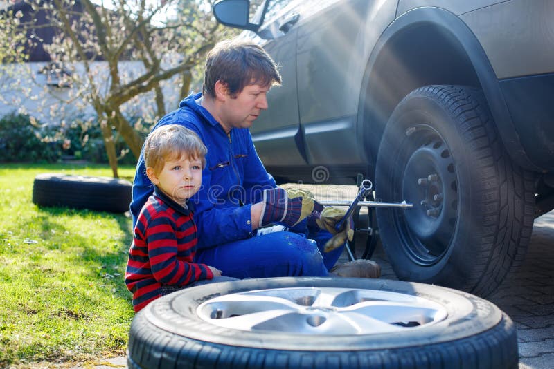 Little kid boy and his father changing wheel on car