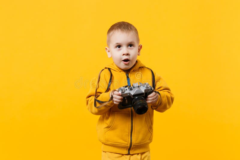 Little kid boy 3-4 years old wearing yellow clothes hold camera isolated on orange wall background, children studio