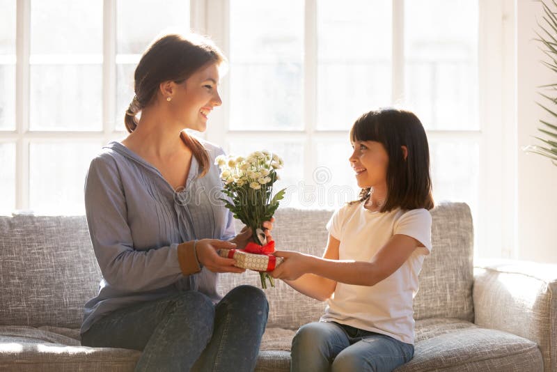 Little kid daughter giving mom receiving gift box and flowers
