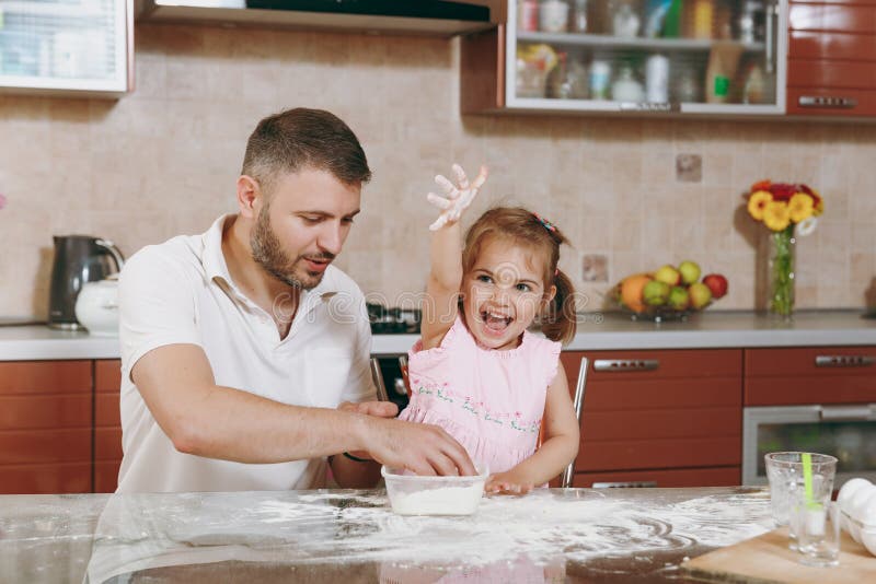 Little kid girl helps man to cook Christmas ginger cookies in kitchen at table. Happy family dad, child daughter cooking