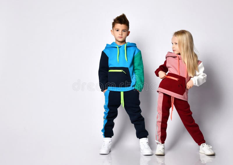 Little kids, boy and girl, in colorful tracksuits and sneakers. They posing isolated on white studio background. Hands in pockets royalty free stock images Little kids, boy and girl, in colorful tracksuits and sneakers. They posing isolated on white studio background. Hands in pockets royalty free stock images