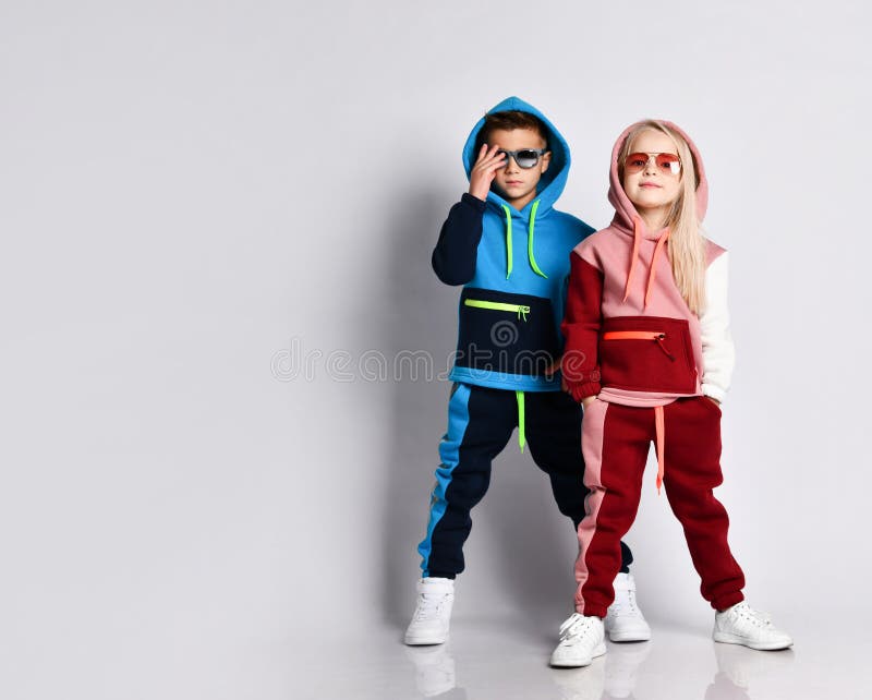 Little kids, boy and girl, in sunglasses and hoods, colorful tracksuits, sneakers. They posing isolated on white studio background stock image Little kids, boy and girl, in sunglasses and hoods, colorful tracksuits, sneakers. They posing isolated on white studio background stock image