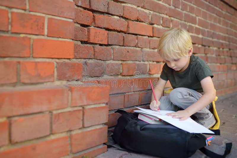 Little pupil doing homework on break near school building. Back to school concept royalty free stock images Little pupil doing homework on break near school building. Back to school concept royalty free stock images