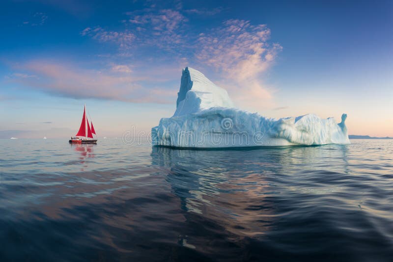 Little red sailboat cruising among floating icebergs in Disko Bay glacier during midnight sun season of polar summer. Greenland