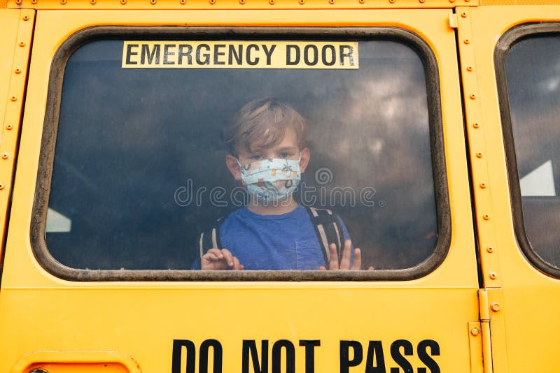 Little sad boy kid student in protective face mask looking out of school yellow bus window. New normal at coronavirus covid-19 royalty free stock images Little sad boy kid student in protective face mask looking out of school yellow bus window. New normal at coronavirus covid-19 royalty free stock images