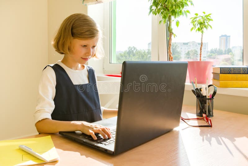 Little schoolgirl uses computer laptop sitting at a desk at home. School, education, knowledge and children stock photography Little schoolgirl uses computer laptop sitting at a desk at home. School, education, knowledge and children stock photography