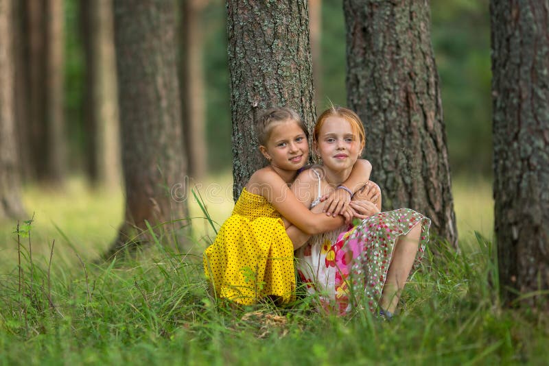 Little sisters are sitting near a tree in the Park. Nature.