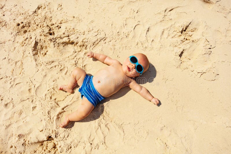 Little toddler baby laying on the sand of beach