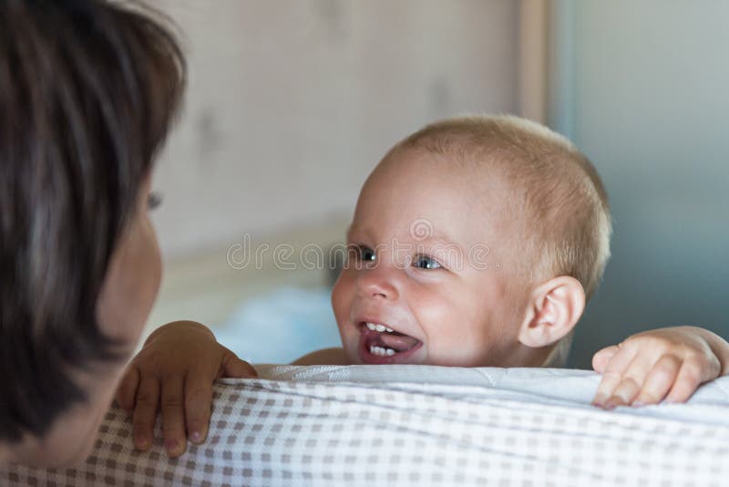 Little toddler boy playing on the bed. Cute kid smiling and hiding under cover. Palyful and mischievous eyes. Hide-and-seek.