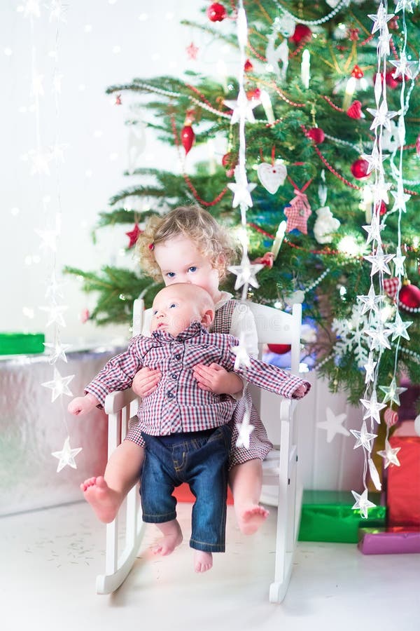 Little toddler girl and her newborn baby brother under Christmas tree stock photo Little toddler girl and her newborn baby brother under Christmas tree stock photo