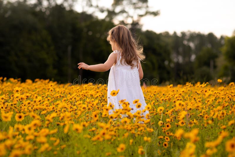 Little Toddler Girl in a White Dress Picking Flowers in a Black