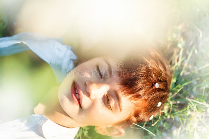 Little 7 years old smiling girl with closed eyes and stylish short haircut laying down in grass under blooming cherry tree in stock image Little 7 years old smiling girl with closed eyes and stylish short haircut laying down in grass under blooming cherry tree in stock image