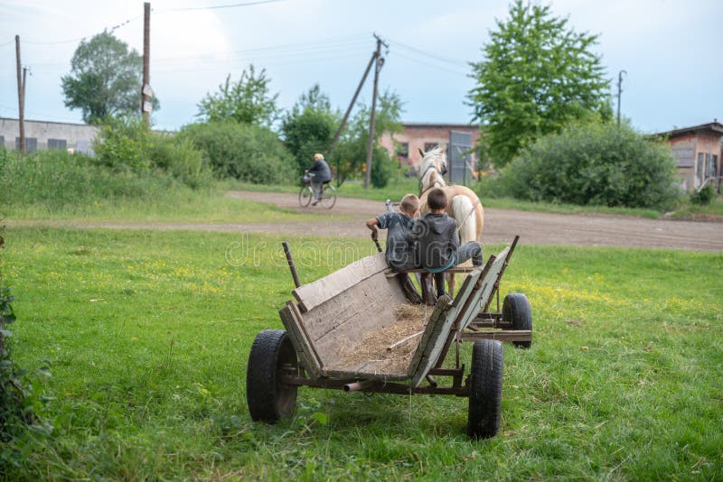Litynia village, Ukraine - June 02, 2018: Two young boys riding on an old wooden cart. Life in a village, lifestyle. Litynia village, Ukraine - June 02, 2018: Two young boys riding on an old wooden cart. Life in a village, lifestyle