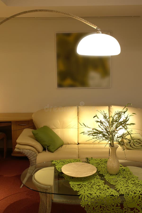 Living room with beige leather couch, coffee table with floral arrangement, green accent pieces and warm, cozy lighting.