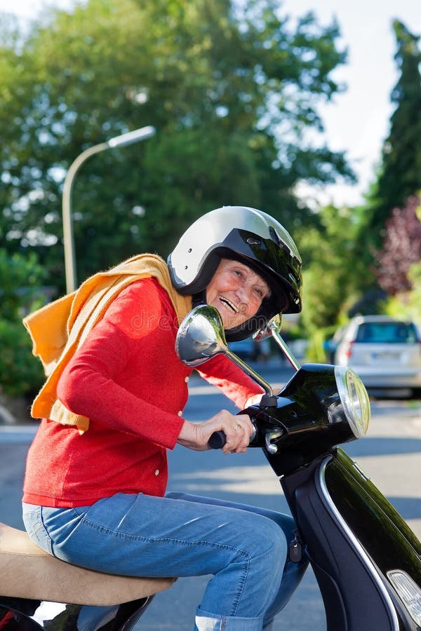 Livlig äldre kvinna som rider en sparkcykel arkivbild Livlig äldre kvinna som rider en sparkcykel arkivbild