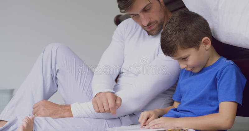 Livre d'histoire de lecture de père et de fils dans la chambre à coucher à la maison confortable 4k banque de vidéos