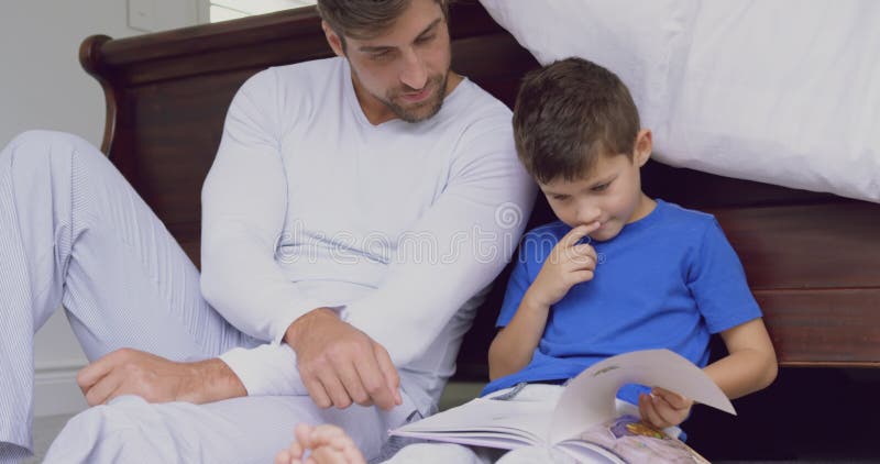 Livre d'histoire de lecture de père et de fils dans la chambre à coucher à la maison confortable 4k clips vidéos