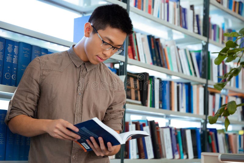 Livre de lecture asiatique d'homme dans la bibliothèque photos stock Livre de lecture asiatique d'homme dans la bibliothèque photos stock