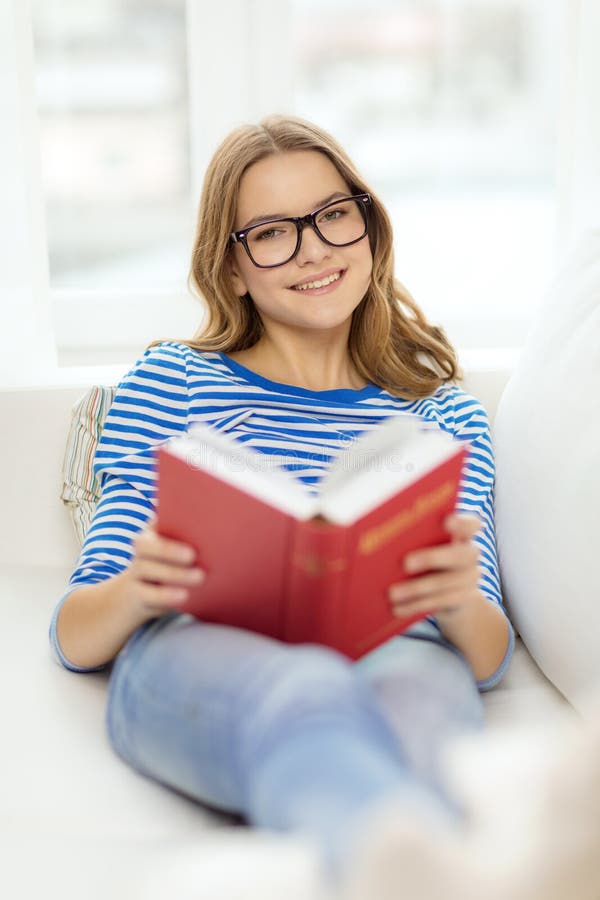 Livre de lecture de sourire d'adolescente sur le divan photographie stock libre de droits