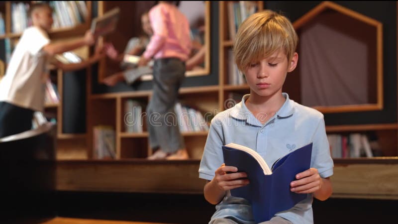 Livre de lecture de garçon attrayant tandis que groupe d'étudiants apprenant derrière. érudition. clips vidéos