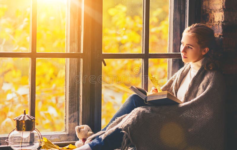 Livre de lecture heureux de femme par la fenêtre d'automne image stock