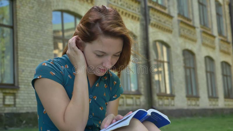 Livre de lecture mignon d'étudiant de gingembre et sourire à l'appareil-photo, se reposant en parc près de l'université, construi clips vidéos