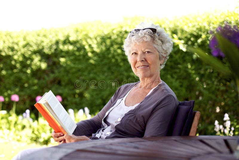 Livre de lecture supérieur heureux de femme dans le jardin photographie stock Livre de lecture supérieur heureux de femme dans le jardin photographie stock