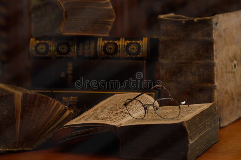 Piles of antique books and open books with reading glasses in a dusty room. Piles of antique books and open books with reading glasses in a dusty room