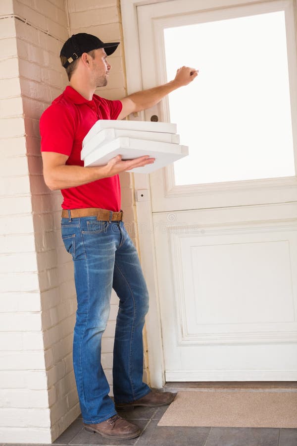 Livreur tenant la pizza tout en frappant sur la porte photographie stock Livreur tenant la pizza tout en frappant sur la porte photographie stock