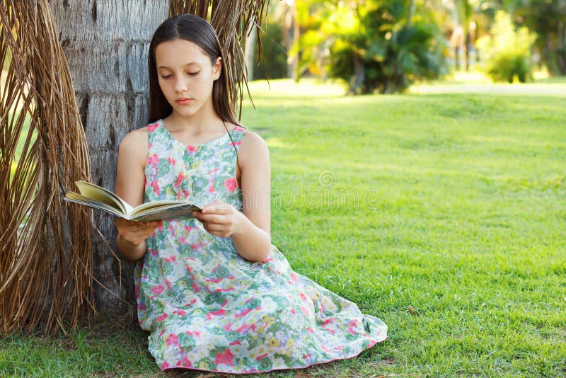 Livro de leitura adolescente bonito da menina que senta-se na grama verde fotografia de stock Livro de leitura adolescente bonito da menina que senta-se na grama verde fotografia de stock