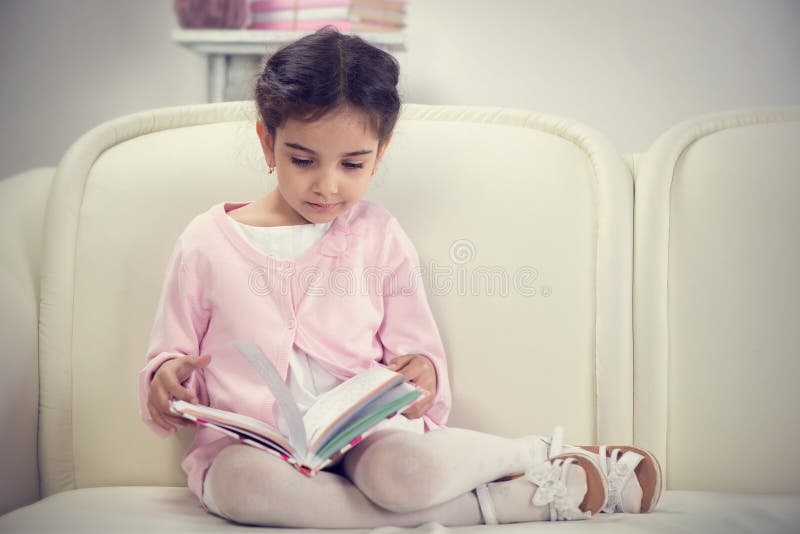 Livro de leitura latino-americano bonito da menina no sofá imagens de stock royalty free Livro de leitura latino-americano bonito da menina no sofá imagens de stock royalty free