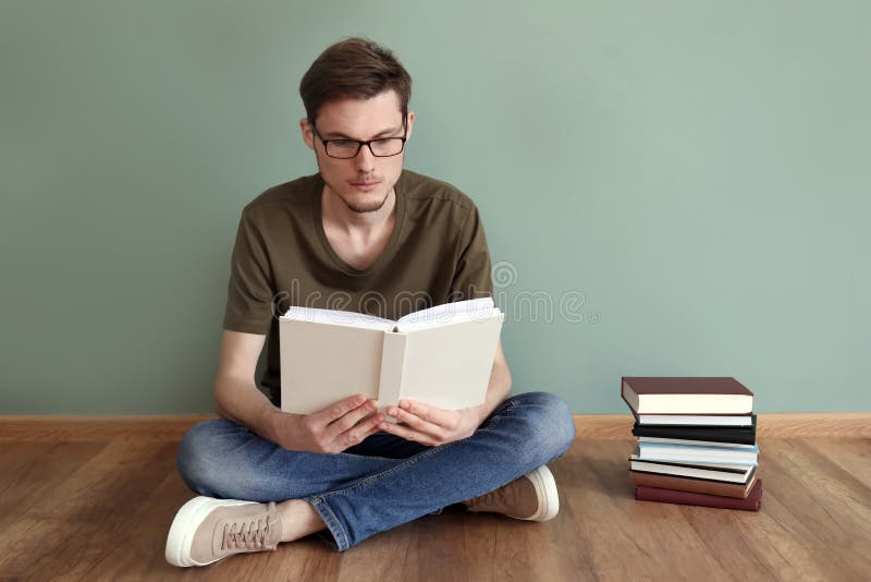 Livros de leitura do homem novo ao sentar-se no assoalho perto da parede da cor fotografia de stock royalty free Livros de leitura do homem novo ao sentar-se no assoalho perto da parede da cor fotografia de stock royalty free